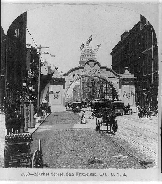 Old photo shows cable cars, pedestrians, and "Welcome" arch on a Market Street, San Francisco, 1899