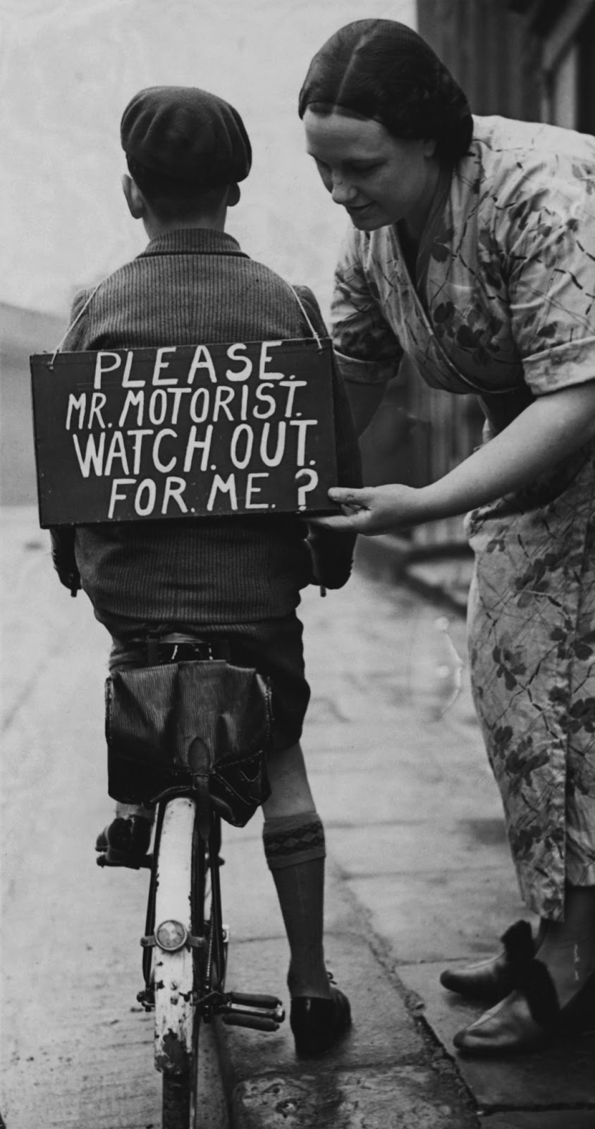 Vintage photo of a mother handing a sign on her son`s back. the sign says "Please Mr Motorist, watch out for me?".