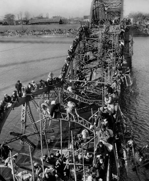 refugees passing destroyed bridge