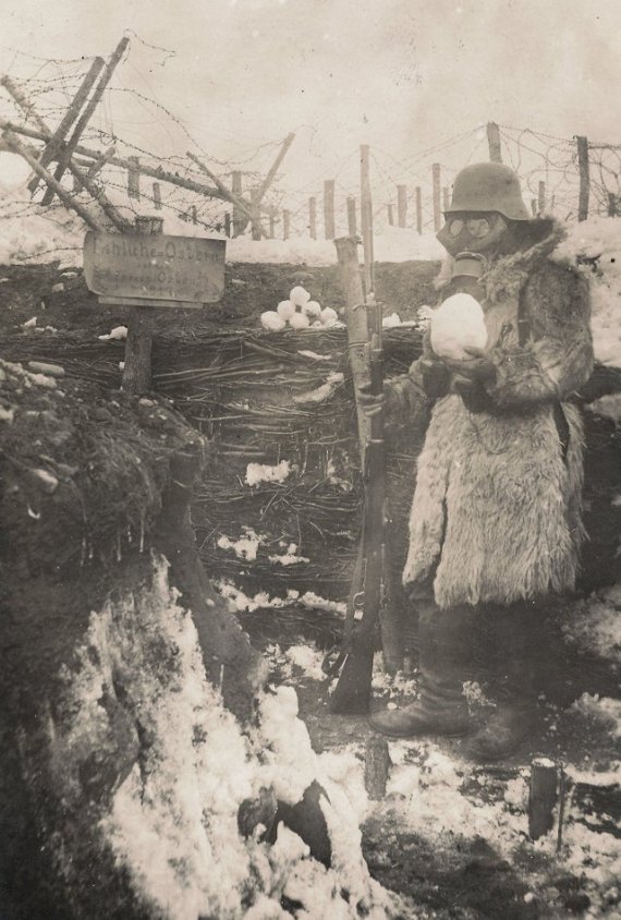 An armed German soldier wearing a gas mask posing with a sign celebrating Easter and an Easter egg snowball in a trench on the Eastern Front, 1917