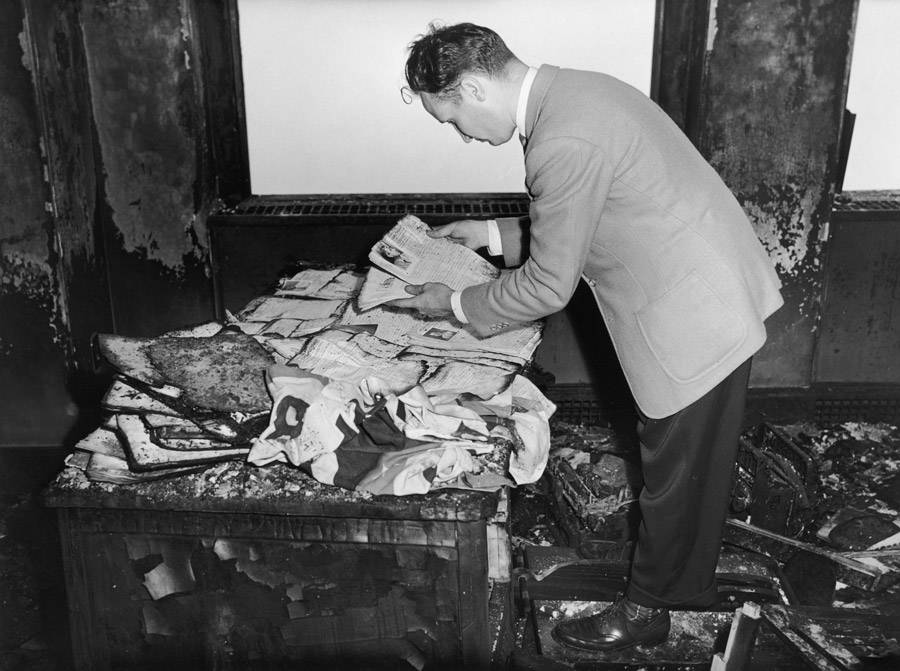 A man examines charred documents in an office in the Empire State Building after a B-25 Bomber crashed into the side of the building. July 28, 1945.