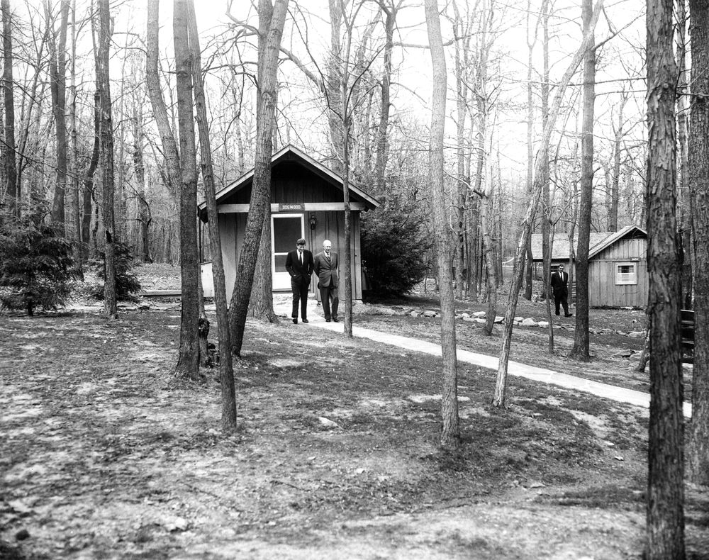 President John F. Kennedy and former President General Dwight D. Eisenhower walk past Dogwood Cabin while talking privately during their meeting at Camp David